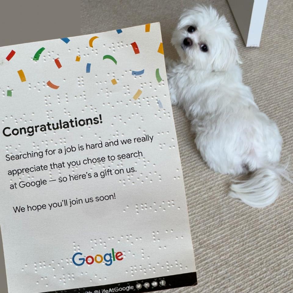 A photo of a congratulatory card from Google held up to the camera, with a white dog in the background