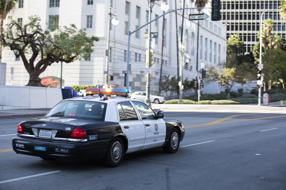 Police car driving on an empty city street near government buildings, palm trees and a landscaped area