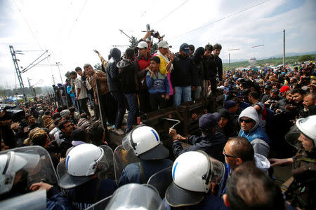 Migrants and refugees are stopped by Greek police after trying to push a train carriage through a police bus on rail tracks leading to Macedonia at a makeshift camp at the Greek-Macedonian border near the village of Idomeni, Greece, April 11, 2016. REUTERS/Stoyan Nenov