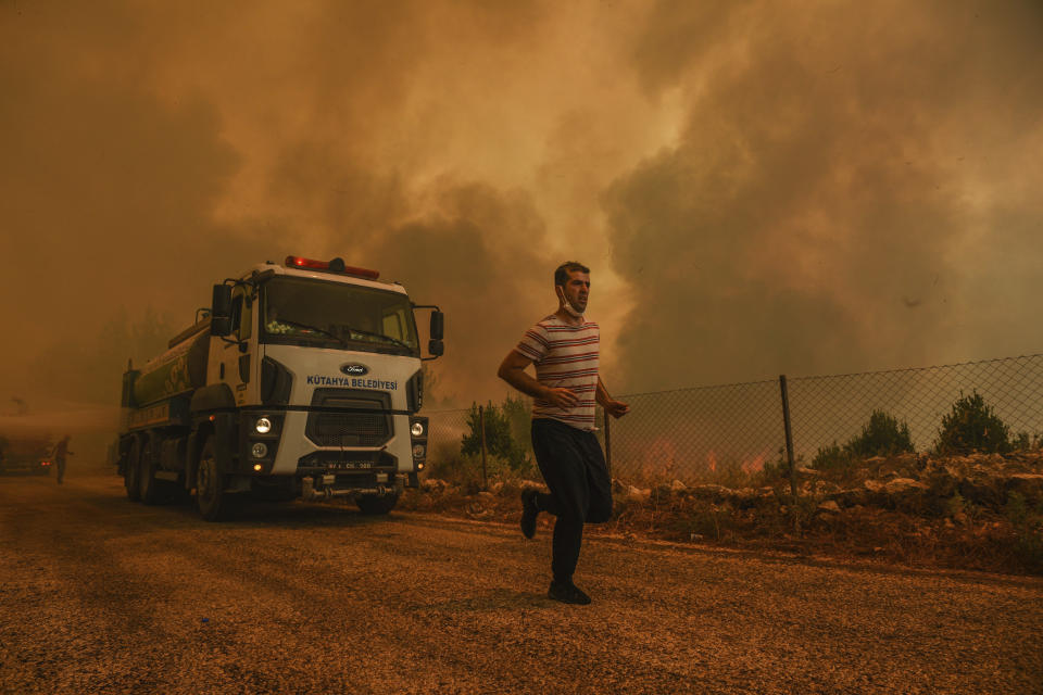 A man runs, in the fire-devastating Sirtkoy village, near Manavgat, Antalya, Turkey, Sunday, Aug. 1, 2021. More than 100 wildfires have been brought under control in Turkey, according to officials. The forestry minister tweeted that five fires are continuing in the tourist destinations of Antalya and Mugla. (AP Photo)