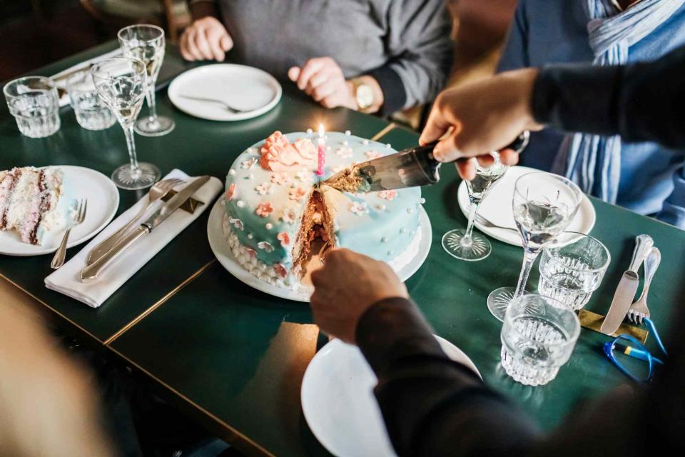 <p>Getty</p> A birthday cake being sliced and served in a restaurant with a group of friends.