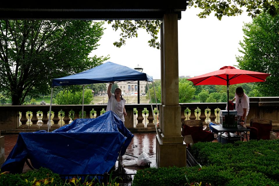 Kirsten Keplar, 45, of Grove City, and Bradley Hart, 33, of Newark, set up picnic umbrellas with prime firework-viewing locations along the Scioto Mile in Downtown Columbus Monday as rain falls prior to Red, White & Boom.