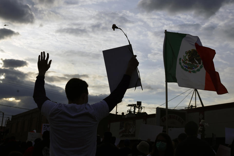 A demonstrator is silhouetted while raising his hands as he attends a peace walk honoring the life of police shooting victim Adam Toledo, 13, Sunday, April 18, 2021, in Chicago's Little Village neighborhood. (AP Photo/Shafkat Anowar)