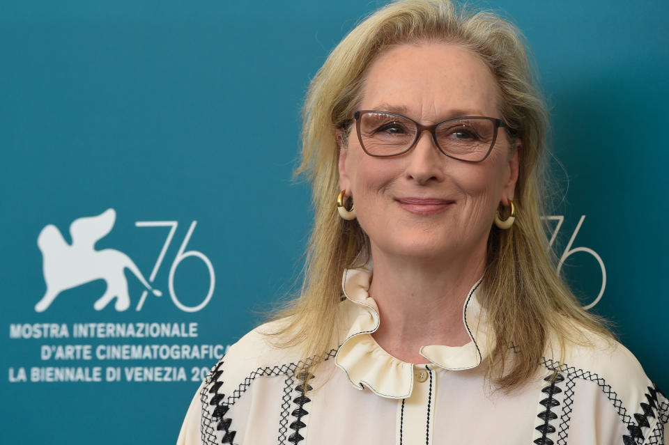 Meryl Streep at an event, smiling, wearing a blouse with ruffled collar and earrings