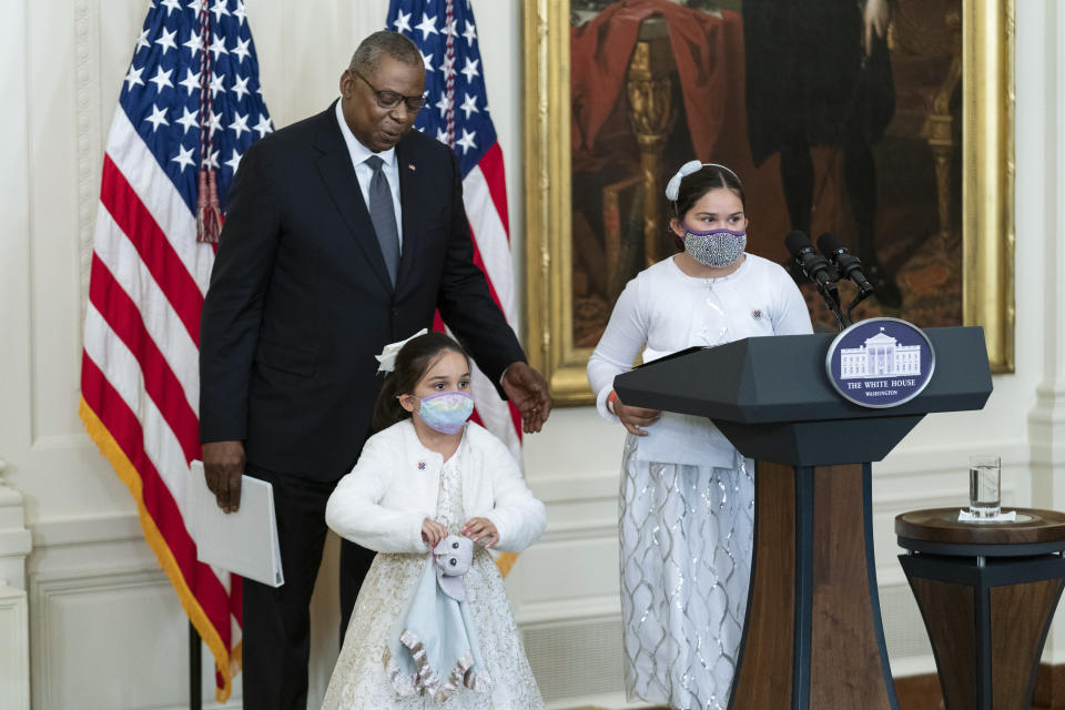 Little caregivers Gabby, right, and Eva Rodriguez, are assisted to the stage in the East Room of the White House by Defense Secretary Lloyd Austin, after introducing them during a ceremony at the White House honoring children in military and veteran caregiving families, Wednesday, Nov. 10, 2021. (AP Photo/Manuel Balce Ceneta)