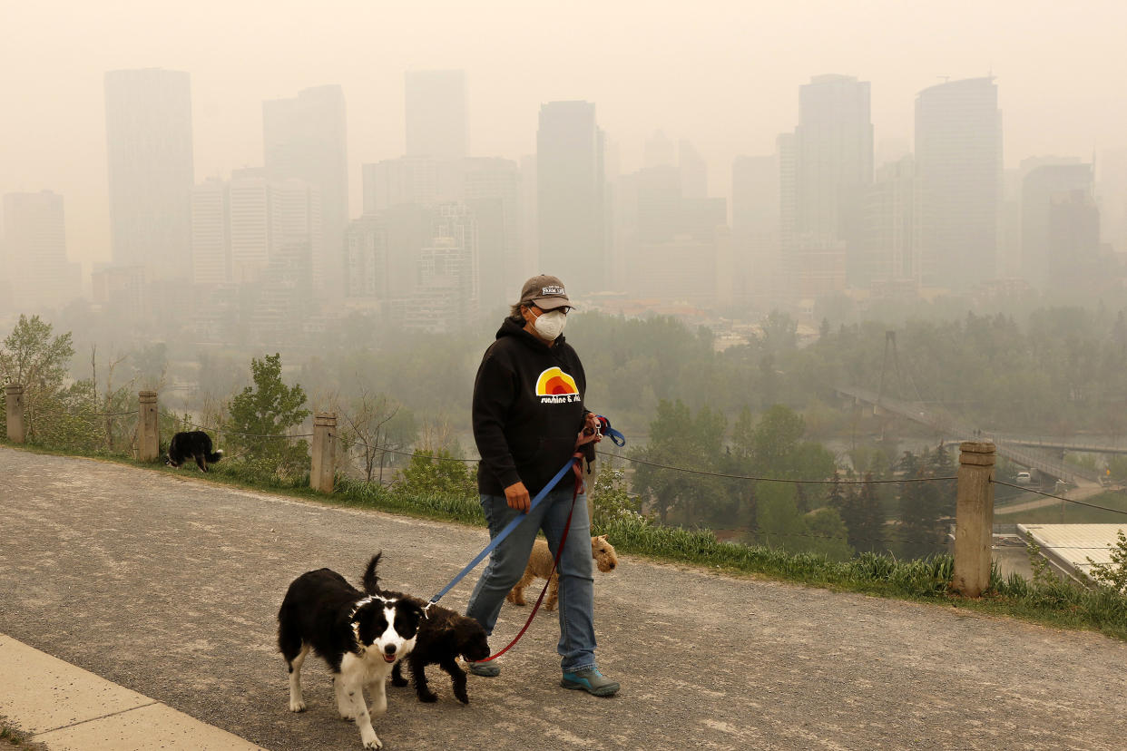 Wearing a protective mask, dog walker Leslie Kramer ventures out as heavy smoke from northern Alberta forest fires comes south to blanket the downtown area in Calgary, Canada, Tuesday, May 16, 2023. (Larry MacDougal/The Canadian Press via AP) (Larry MacDougal / The Canadian Press via AP)