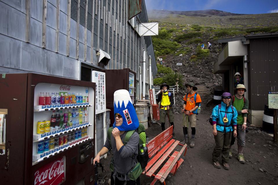 In this Thursday, Aug. 29, 2013 photo, a Japanese man, wearing a Mount Fuji-shaped hat, passes by vending machines and benches at a rest station on one of the trails on Mount Fuji. The recent recognition of the 3,776-meter (12,388-foot) peak as a UNESCO World Heritage site has many here worried that will draw still more people, adding to the wear and tear on the environment from the more than 300,000 who already climb the mountain each year. (AP Photo/David Guttenfelder)