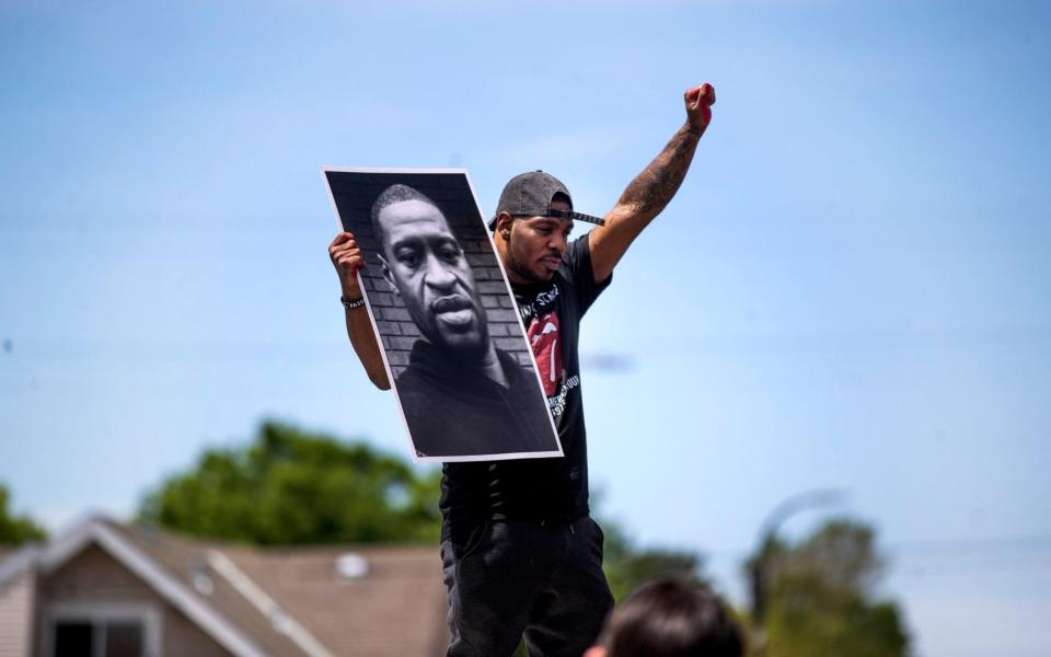 A protester in Minneapolis holds a photo of George Floyd - AP