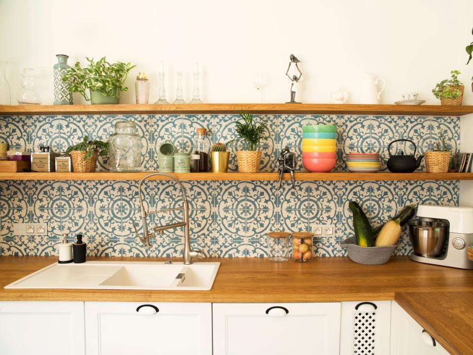 Stylish open space kitchen with accessories, plants and plates. Design interior of cozy kitchen. Mosaic backgrounds wall.