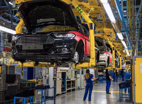 Partially-completed Mondeo sedans are shown in cradles, several feet above the factory floor, with workers underneath.