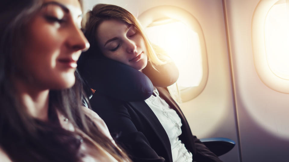 Girlfriends traveling by plane. A female passenger sleeping on neck cushion in airplane