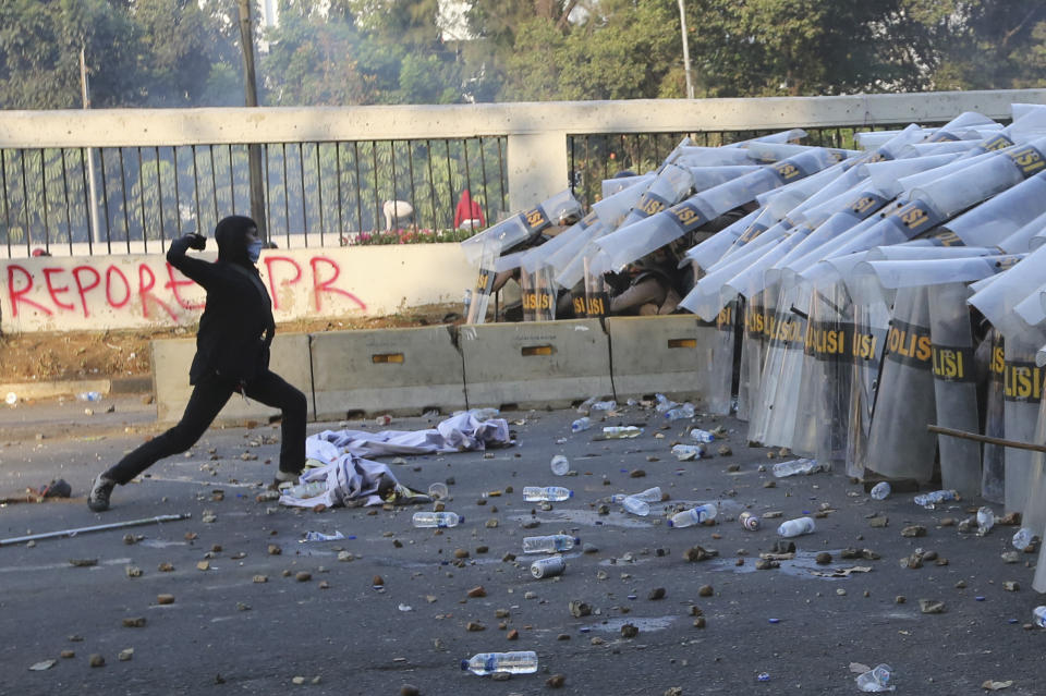 A student protester throws a rock at riot police officers during a clash in Jakarta, Indonesia, Monday, Sept. 30, 2019. Thousands of Indonesian students resumed protests on Monday against a new law they say has crippled the country's anti-corruption agency, with some clashing with police. (AP Photo/Tatan Syuflana)