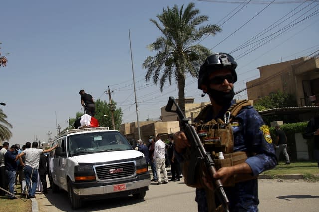 An Iraqi Federal Policeman stands guard while mourners load the flag-draped coffin of Hisham al-Hashimi during his funeral