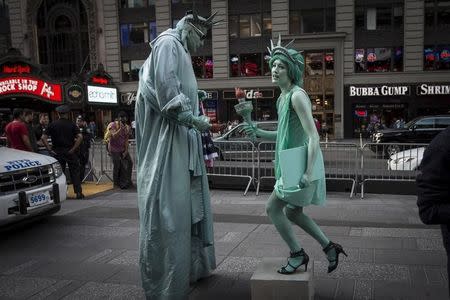 A woman (R) who gave her name as Allyson and is dressed up as the Statue of Liberty teases and harasses a man who is also dressed up as a Statue of Liberty while she films a comedy segment in Times Square in the Manhattan borough of New York October 8, 2015. REUTERS/Carlo Allegri