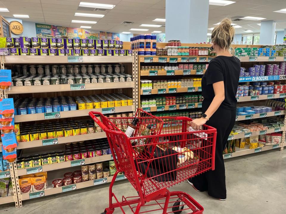 The author holding onto a red shopping cart while standing in front of an aisle at Trader Joe's.