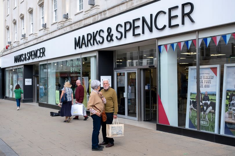 Shoppers outside the front of a Marks & Spencer, including an elderly couple and another couple walking by with multiple bags