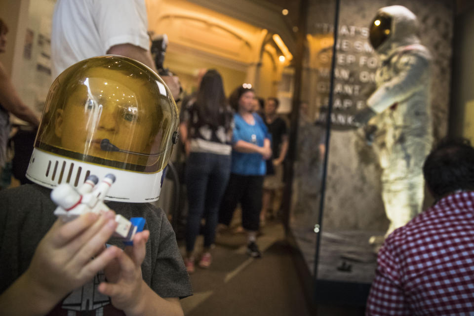 Jack Heely, 5, of Alexandria, Va., wears a toy space helmet as he arrives as one of the first visitors to view Neil Armstrong's Apollo 11 spacesuit, background, after it is unveiled at the Smithsonian's National Air and Space Museum on the National Mall in Washington, Tuesday, July 16, 2019. (AP Photo/Andrew Harnik)