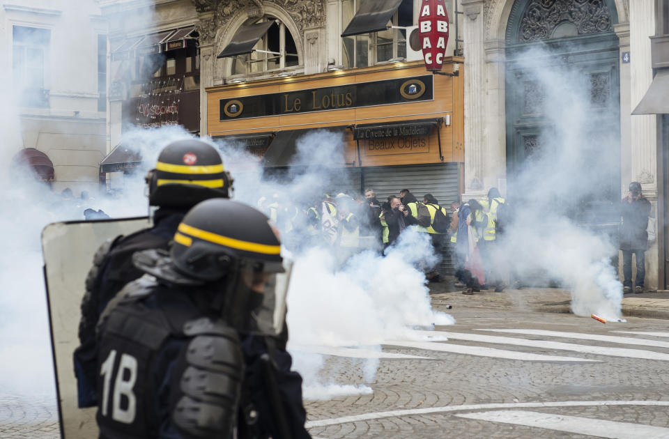 Riot police officers fire tear gas at demonstrators wearing yellow vests near the Madeleine church in Paris Saturday, Dec. 22, 2018. A few hundred protesters cordoned by the police did walk across Paris toward the Madeleine Church near the Elysee Palace but were stopped by police in a small adjacent street as some shop owners closed down early. Tempers frayed and police fired tear gas to repel protesters trying to break through the officers' line. (AP Photo/Kamil Zihnioglu)