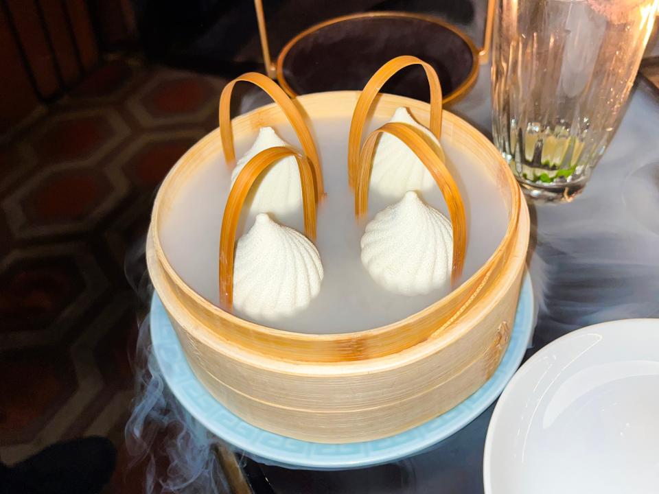 A steamer filled with ice cream shaped like white dumplings. Steam spills out of the steamer serving tray.