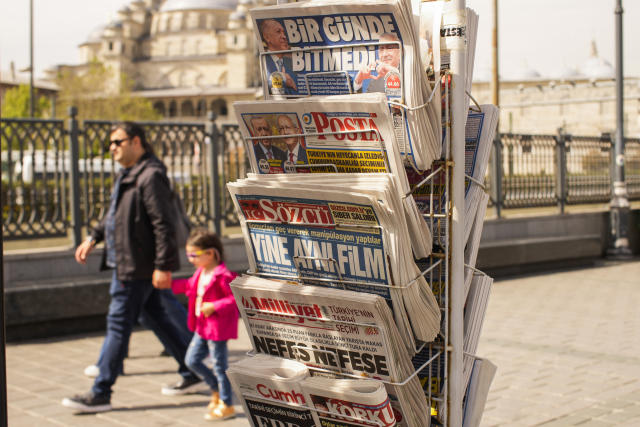 People walk past a rack with Turkish newspapers a day after the presidential election day, in Istanbul, Turkey, Monday, May 15, 2023. Turkey's presidential elections appeared to be heading toward a second-round runoff on Monday, with President Recep Tayyip Erdogan, who has ruled his country with a firm grip for 20 years, leading over his chief challenger, but falling short of the votes needed for an outright win. (AP Photo/Emrah Gurel)
