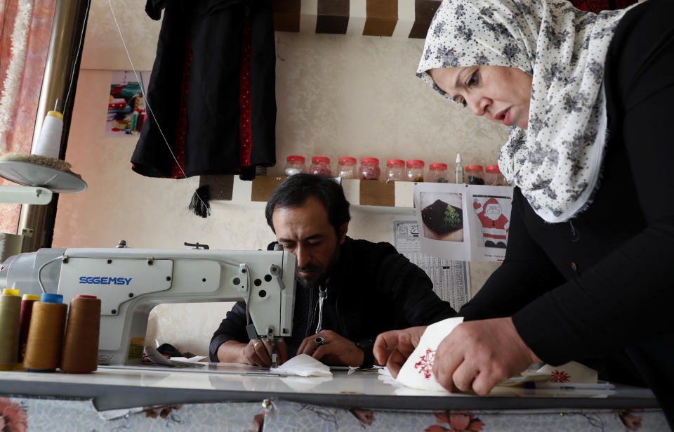 Suhad Saidam, works with a tailor on Christmas face masks at her sewing workshop in Gaza City, Monday, Dec. 14, 2020. In the blockaded Gaza Strip, the Christmas season is giving a boost to Saidam's business that produces pandemic face masks decorated with holiday symbols. And they have found markets as far away as Europe. (AP Photo/Adel Hana)