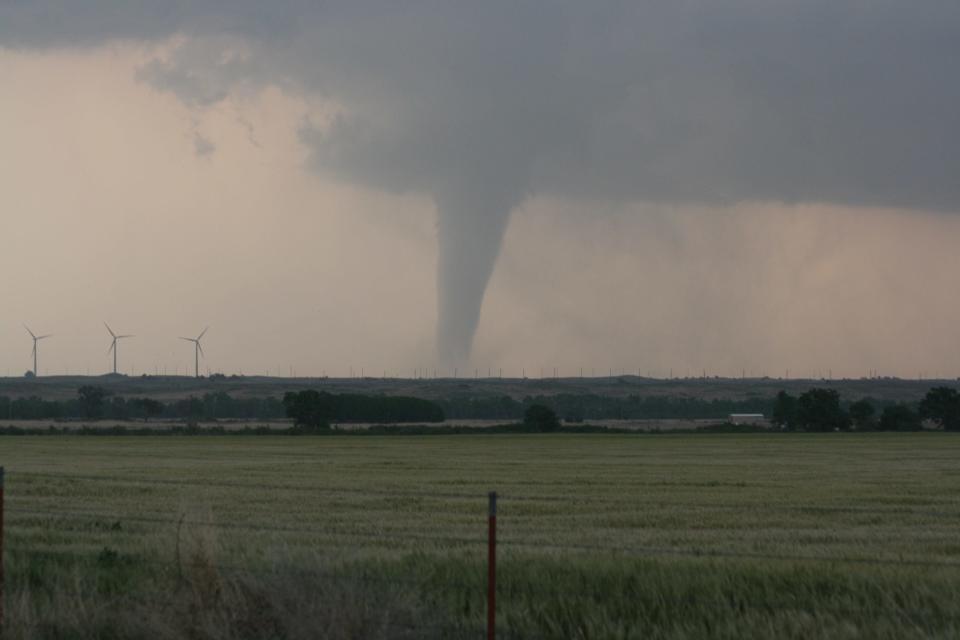 A tornado by some wind turbines with a field in front