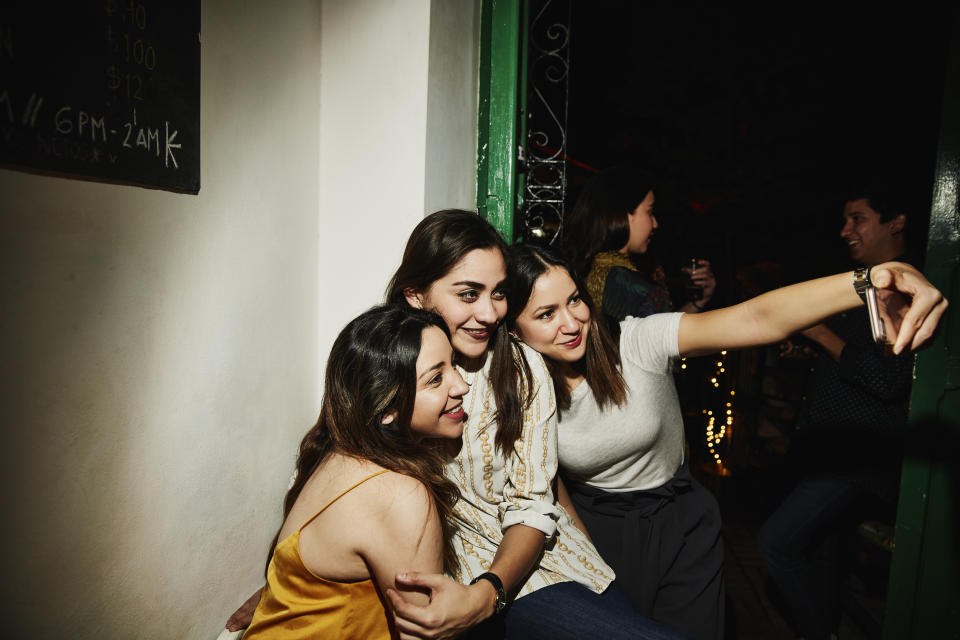 Smiling female friends taking selfie with smart phone while hanging out in night club