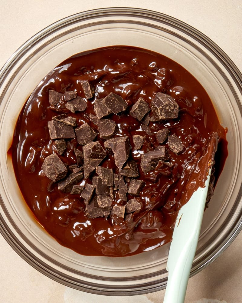 Overhead shot of semi melted chocolate in a glass bowl with a blue spatula resting in the bowl.