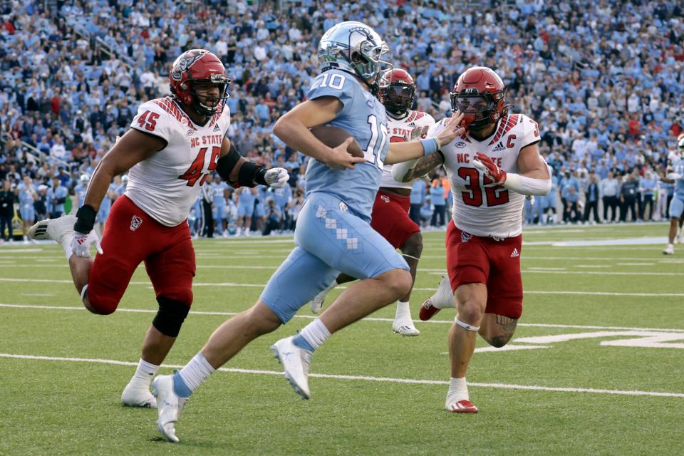 North Carolina quarterback Drake Maye (10) is pursued by North Carolina State defensive tackle Davin Vann (45) and linebacker Drake Thomas (32) as he runs upfield during the first half of an NCAA college football game Friday, Nov. 25, 2022, in Chapel Hill, N.C. (AP Photo/Chris Seward)