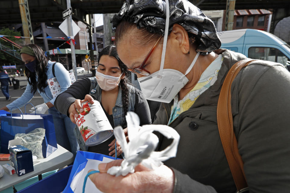 Sistas Van driver Denise Rodriguez, center, adds a can of tomato juice to a woman's bag after the woman waited in line to receive free food and other donations the group was giving away to those in need at Brooklyn's Broadway Triangle amid the coronavirus outbreak, Tuesday, May 19, 2020, in New York. (AP Photo/Kathy Willens)