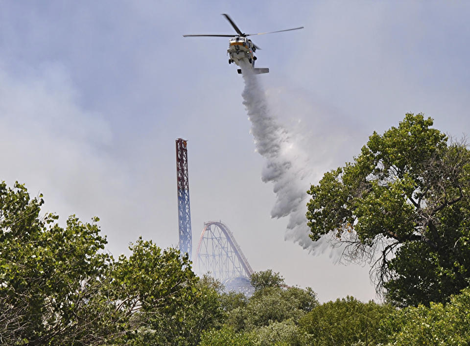 Los Angeles County Fire helicopter drops water on brush fire burning close to Six Flags Magic Mountain and Hurricane Harbor amusement park in Santa Clarita, Calif., Sunday, June 9, 2019. Heavy smoke surrounding Six Flags Magic Mountain and Hurricane Harbor prompted the park to announce an evacuation shortly after noon Sunday north of Los Angeles. But about 40 minutes later, the park said on its Twitter account that fire officials asked guests to stay at the park while they work to contain the blaze. Police closed access roads to the park off Interstate 5. (AP Photo/Rick McClure)