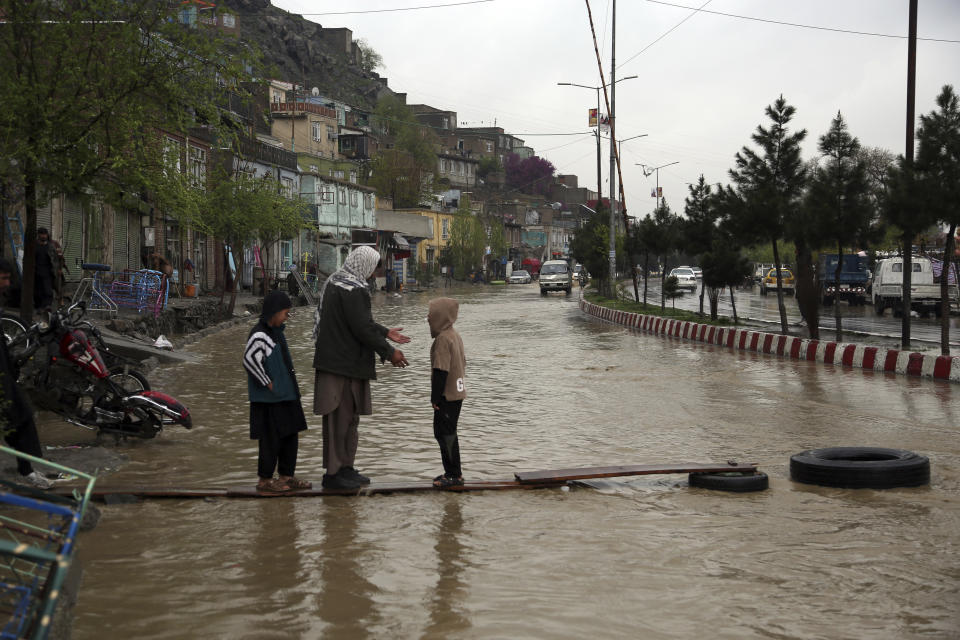 An Afghan man walks with his children through floodwaters as heavy rain falls in Kabul, Afghanistan, Tuesday, April 16, 2019. Afghan officials say at least five more people have been killed and 17 are missing as a new wave of heavy rains and flooding swept across the country's western Herat province. (AP Photo/Rahmat Gul)