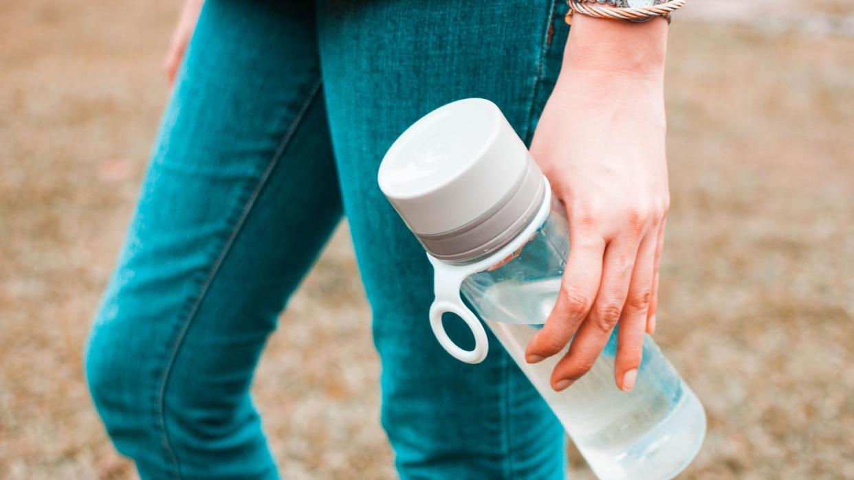a young woman is holding a reusable water bottle container outdoors