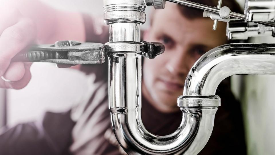 Plumber using a wrench to tighten a siphon under a sink.