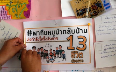 A well-wisher pins up a poster praying for the safety of the boys and their coach, saying: "take Wild Boars back home" - Credit: AP Photo/Sakchai Lalit