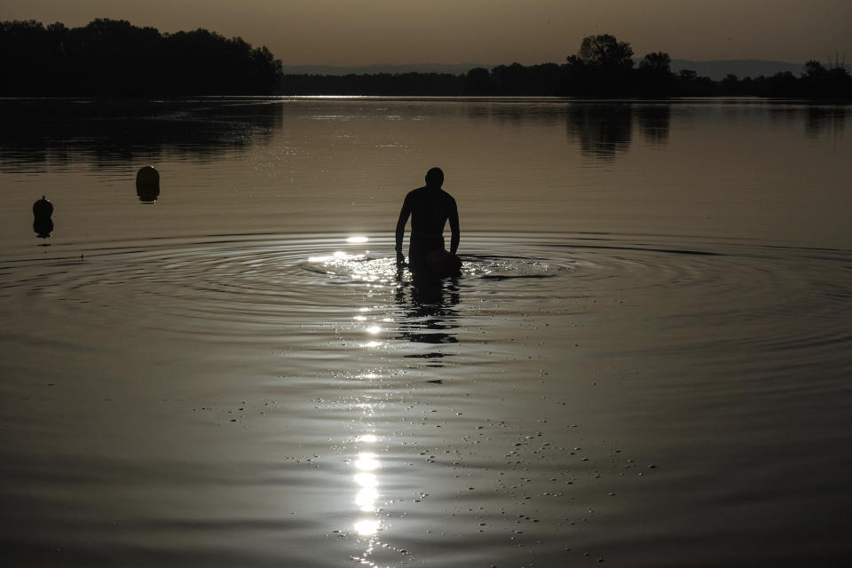 FILE - A man walks in the water as the sun rises above the Miribel lake, outside Lyon, central France, Saturday, June 18, 2022. A heat wave that's already lasted more than a week keeps on baking the US, Asia, Europe and even the Arctic. (AP Photo/Laurent Cipriani, File)