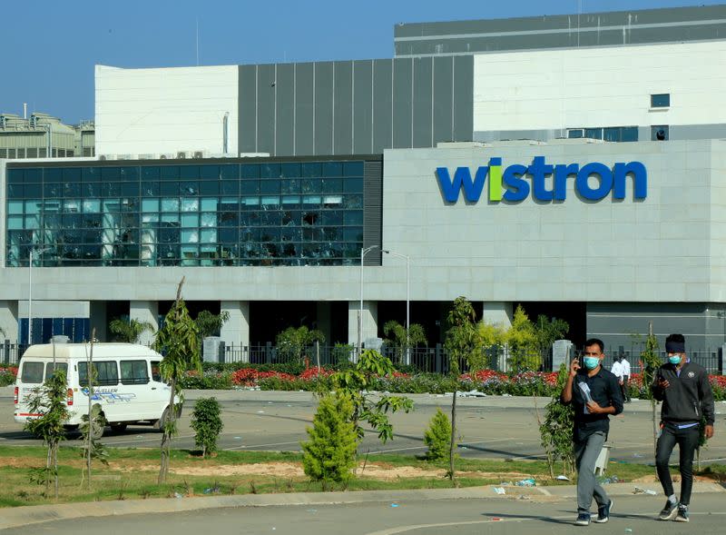 FILE PHOTO: Men wearing protective face masks walk past broken windows of a facility run by Wistron Corp in Narsapura, southern India
