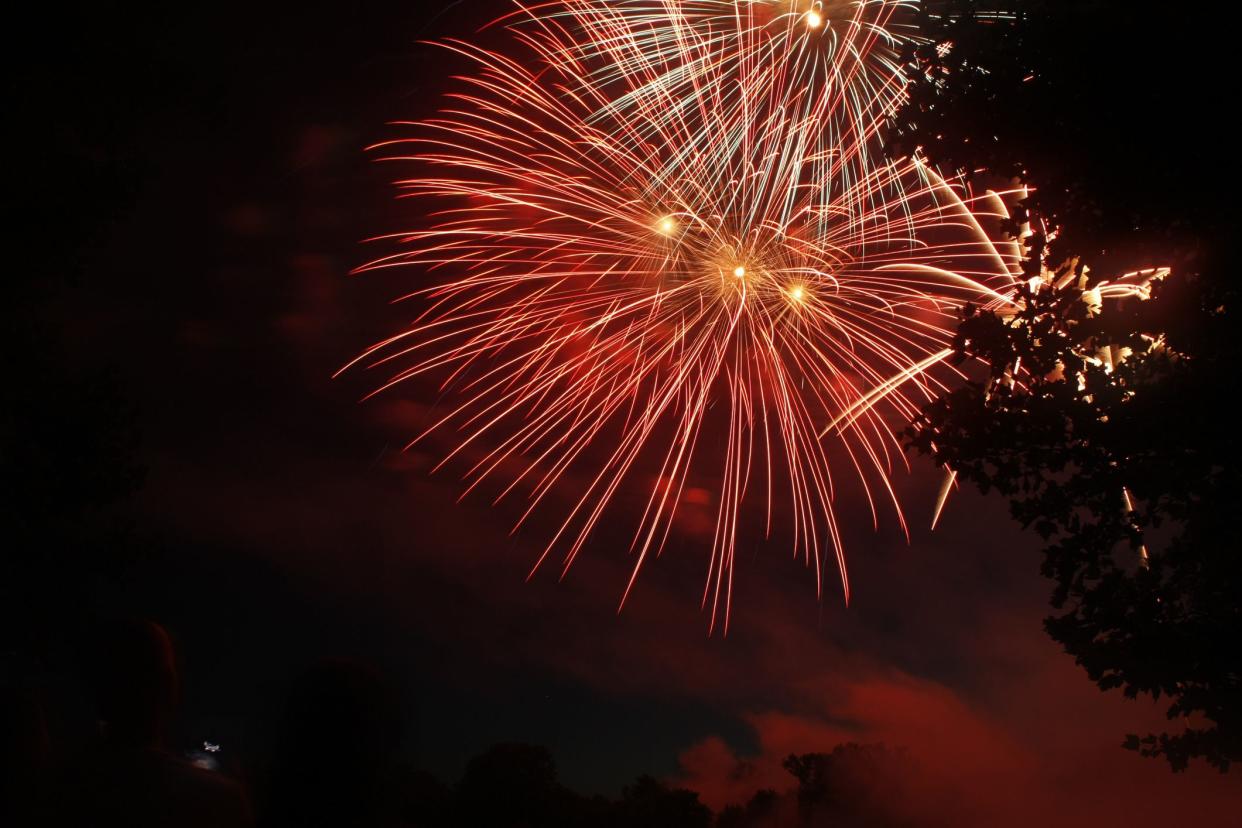 Fireworks display on july 4th lighting up the night sky to red. A person is seen on the bottom left of this image viewing the display.