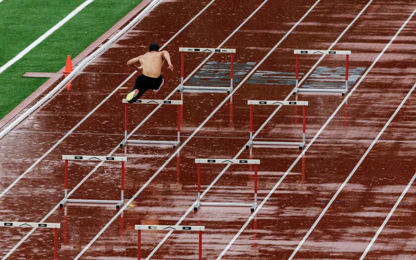 RIVERSIDE, CA - FEBRUARY 20, 2024: A shirtless member of the track team practices the hurdles in the pouring rain on a wet track at Riverside City College on February 20, 2024 in Riverside, California.(Gina Ferazzi / Los Angeles Times)