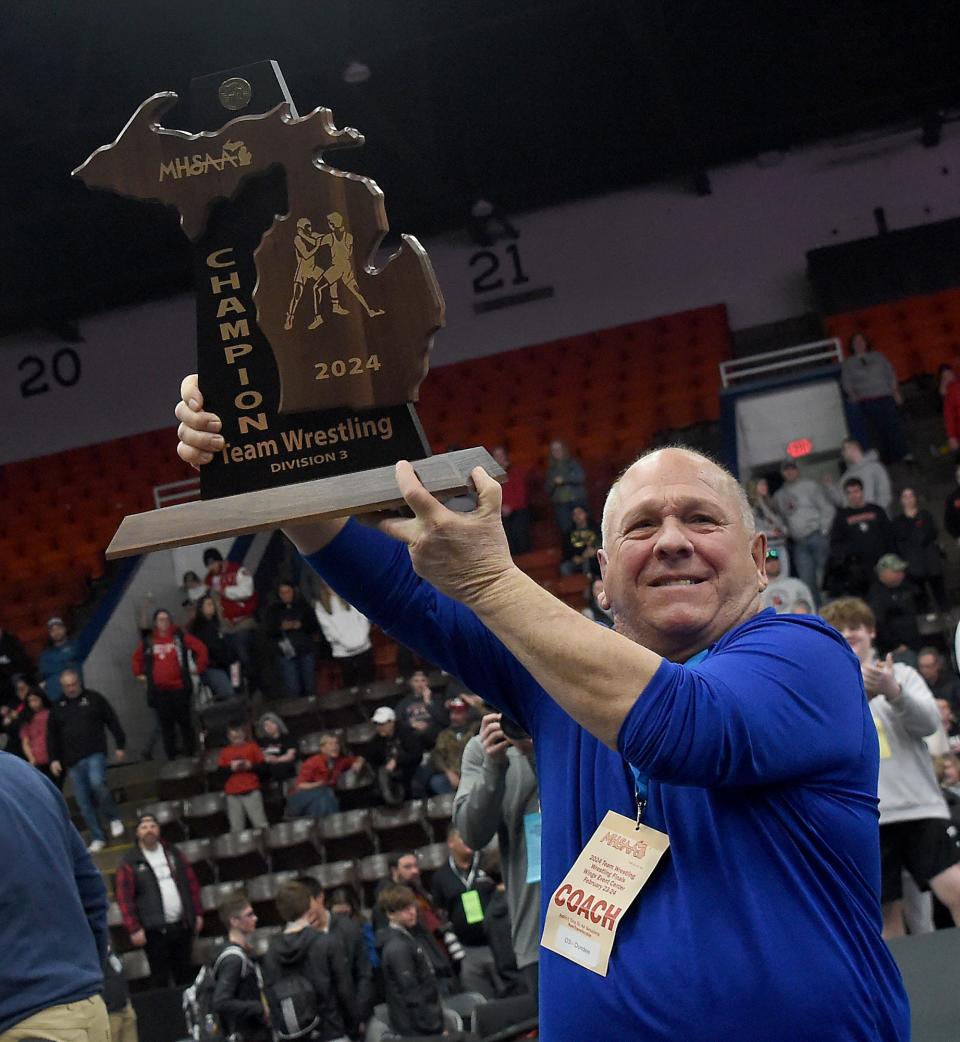 Long-time youth coach Ron Silveira accepts the state championship trophy after Dundee beat Whitehall 49-20 n the Division 4 state team at the Wings Event Center in Kalamazoo Saturday, Feb. 24, 2024.