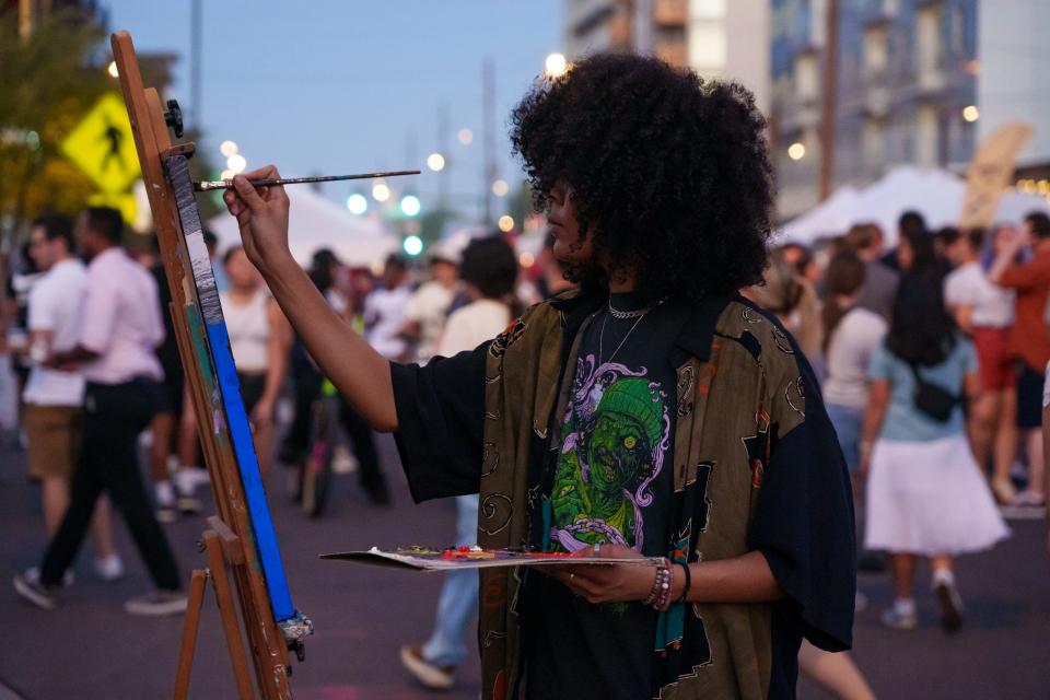 Shyla Ferrell paints as people fill the street for the First Friday Artwalk on Roosevelt Row on August 4, 2023 in Downtown Phoenix, AZ.