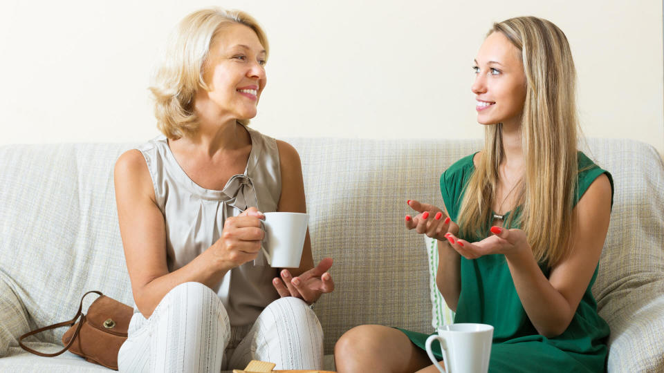 Happy mature mother and adult daughter gossiping on sofa at home.