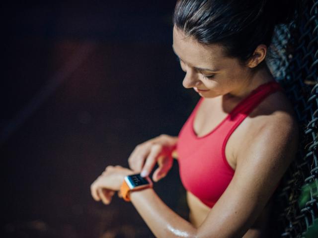 An athlete in a red sports bra checking a wrist heart rate monitor during a workout
