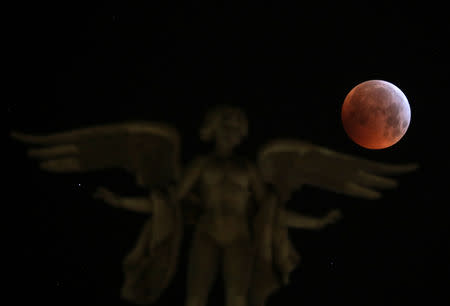 The moon is seen over "Victoria Alada" statue on the top of Metropoli building during a total lunar eclipse, known as the "Super Blood Wolf Moon" in Madrid, Spain, January 21, 2019. REUTERS/Sergio Perez