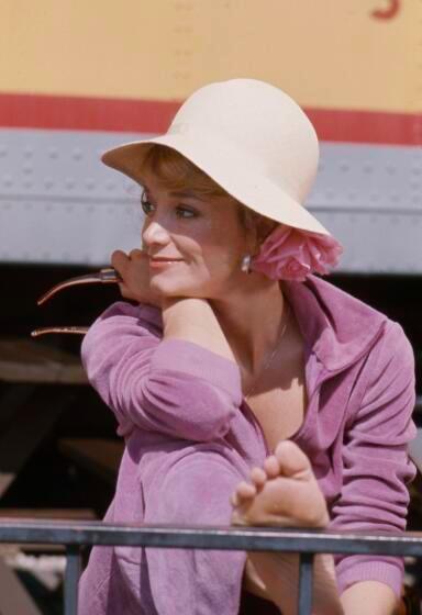 Lynne Marta, in a hat, has a relaxed smile as she rests her head on her arm, her outstretched foot rests on a metal rail