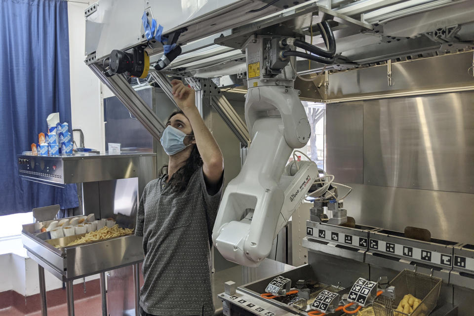 A technician makes an adjustment to a robot at Miso Robotics' White Castle test kitchen in Pasadena, Calif., Thursday, July 9, 2020. Robots that can flip burgers, make salads and even bake bread are in growing demand as virus-wary kitchens try to put some distance between workers and customers. Starting this fall, the White Castle burger chain will test the robot arm that can cook french fries and other foods. The robot, dubbed Flippy, is made by Pasadena, California-based Miso Robotics. (Miso Robotics via AP)