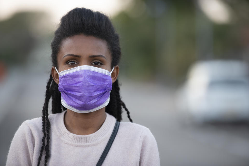 Young Ethiopian woman wearing a face mask, standing outdoors, looking at the camera.