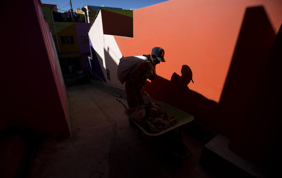 In this May 31, 2019 photo, a worker hauls debris in the Chualluma neighborhood, in La Paz, Bolivia. Residents of a poor neighborhood of the Bolivian capital decorate their humble homes by painting their walls with murals that depict indigenous Aymara women selling produce in the streets, hummingbirds and other colorful images that stand out from the red brick huts. (AP Photo/Juan Karita)