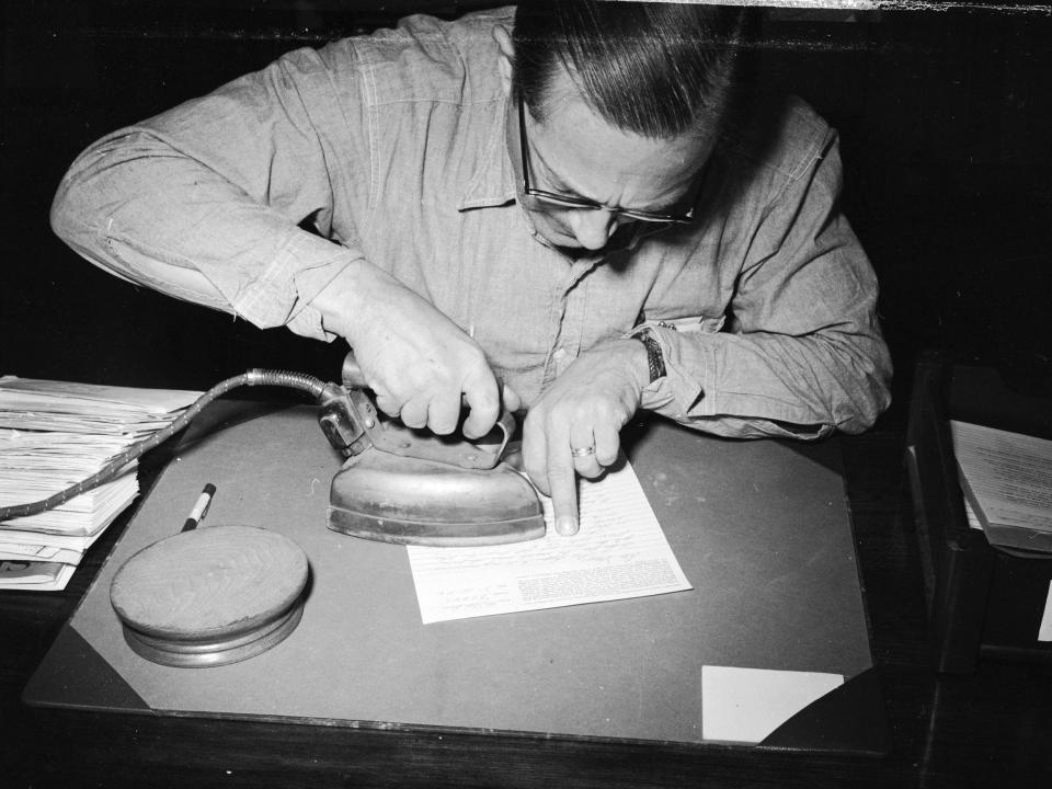 William Abel, a mail censor at Iowa's State Prison, Fort Madison, using a hot iron to bring out a secret message written in lemon juice on a letter.