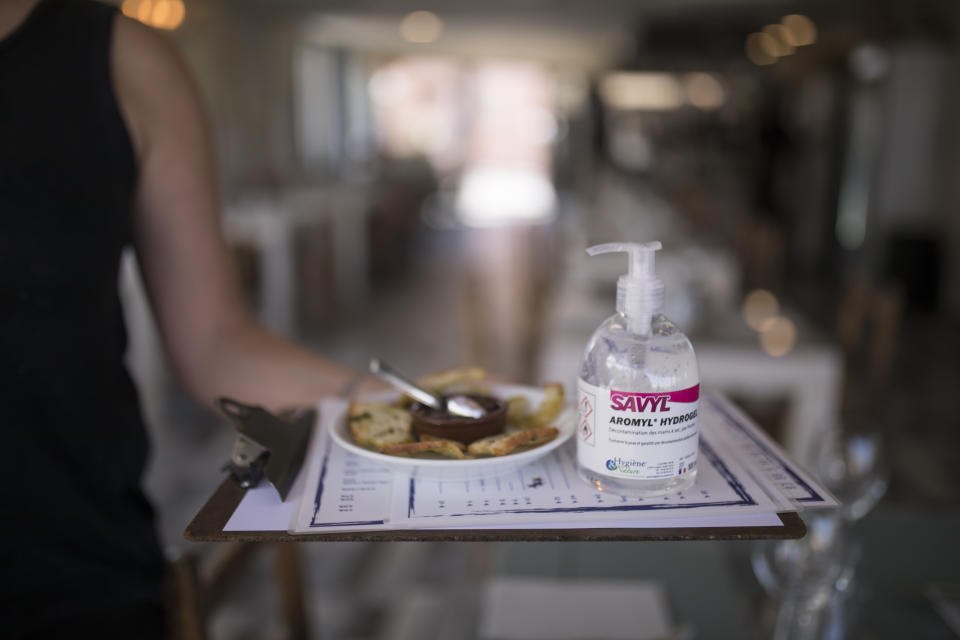 A waitress carries menus and hand sanitizer at a seafood restaurant in Marseille, southern France, Tuesday, June 2, 2020. The French way of life resumes Tuesday with most virus-related restrictions easing as the country prepares for the summer holiday season amid the pandemic. (AP Photo/Daniel Cole)